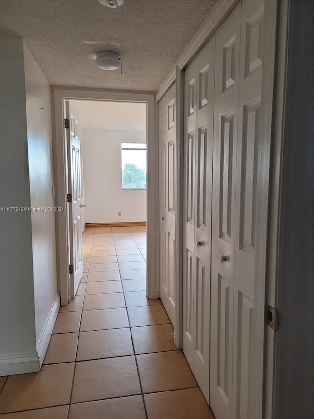 hallway with crown molding, a textured ceiling, and light tile patterned floors