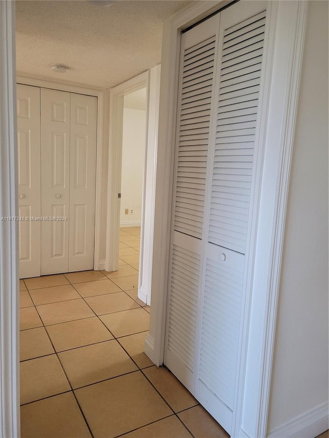 hall with a textured ceiling and light tile patterned floors