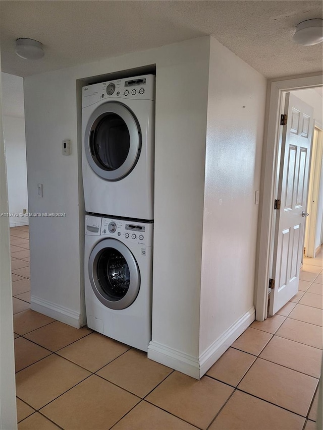 laundry room with a textured ceiling, light tile patterned floors, and stacked washing maching and dryer