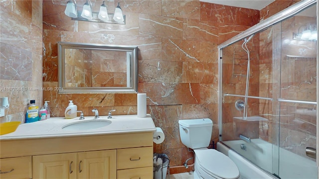 full bathroom with vanity, toilet, tile walls, and bath / shower combo with glass door