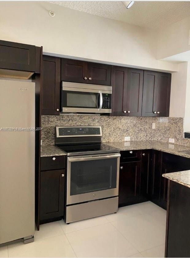 kitchen featuring light stone counters, stainless steel appliances, dark brown cabinetry, and tasteful backsplash