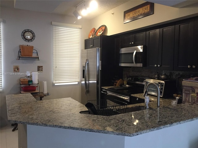 kitchen featuring stainless steel appliances, light stone countertops, track lighting, and kitchen peninsula