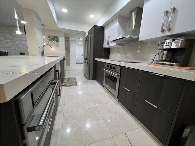 kitchen with wall chimney range hood, decorative backsplash, appliances with stainless steel finishes, white cabinetry, and sink