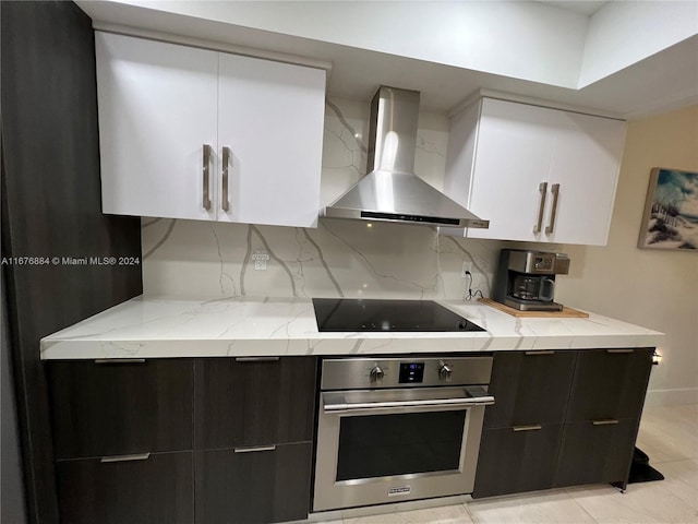 kitchen featuring black electric cooktop, wall chimney exhaust hood, oven, backsplash, and white cabinets