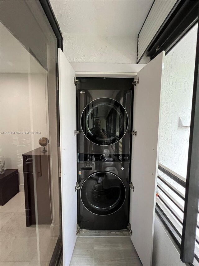 clothes washing area featuring light tile patterned flooring and stacked washer / dryer