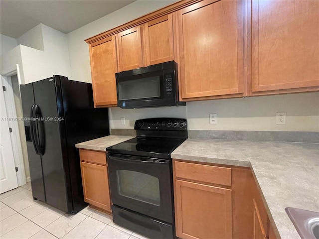 kitchen featuring light tile patterned floors, brown cabinetry, light countertops, and black appliances