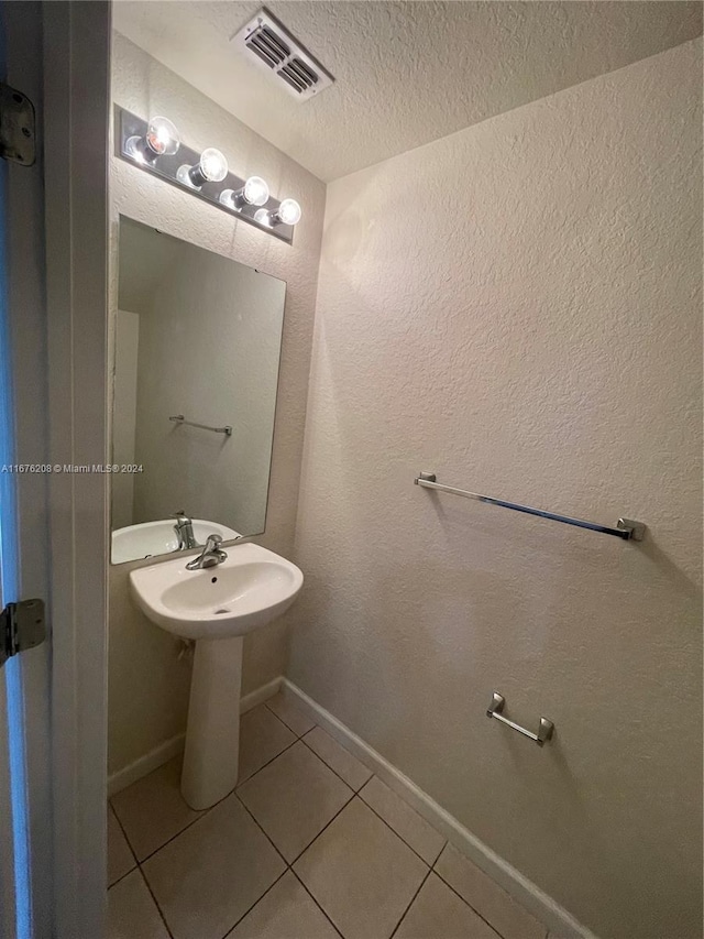 bathroom with a textured ceiling, a textured wall, baseboards, tile patterned flooring, and visible vents