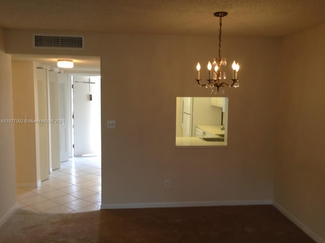 empty room featuring a notable chandelier, a textured ceiling, and light tile patterned floors