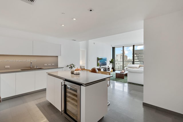 kitchen with a kitchen island, sink, white cabinets, beverage cooler, and floor to ceiling windows