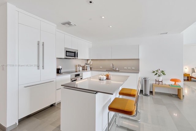 kitchen with a breakfast bar, sink, a center island, appliances with stainless steel finishes, and white cabinets