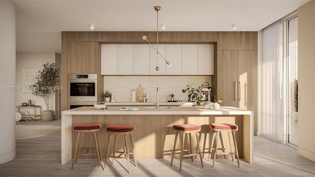 kitchen with sink, decorative light fixtures, a kitchen island with sink, light hardwood / wood-style flooring, and a breakfast bar area