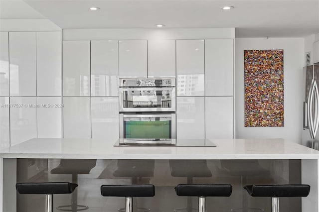 kitchen featuring a breakfast bar, appliances with stainless steel finishes, white cabinetry, and light stone counters