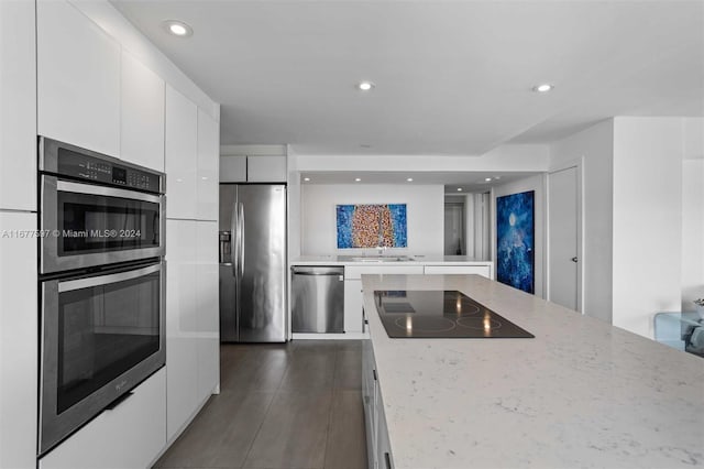 kitchen featuring light stone countertops, sink, dark wood-type flooring, stainless steel appliances, and white cabinets