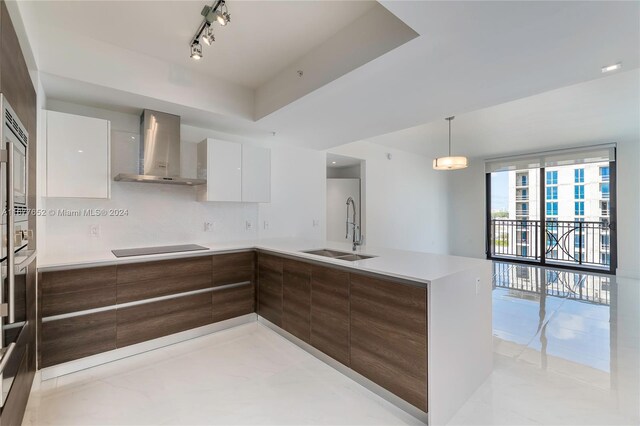 kitchen featuring wall chimney range hood, white cabinetry, black electric cooktop, sink, and decorative light fixtures