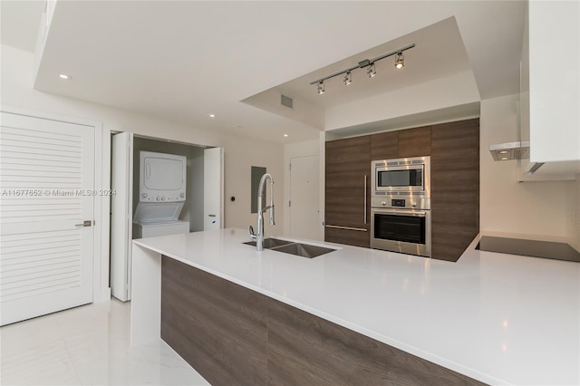 kitchen with sink, kitchen peninsula, stainless steel appliances, dark brown cabinetry, and stacked washing maching and dryer