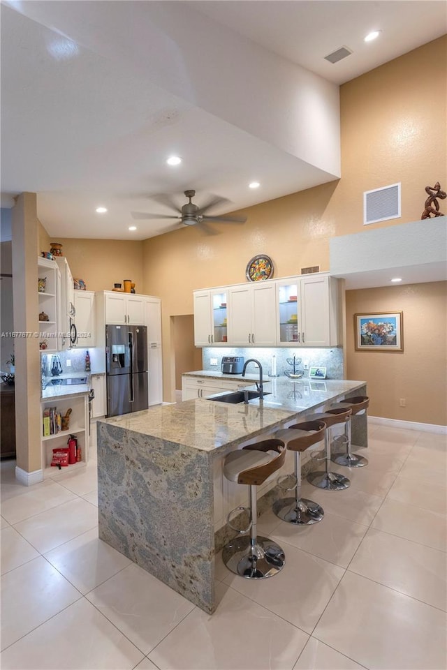 kitchen featuring light stone countertops, stainless steel fridge, white cabinets, and light tile patterned flooring