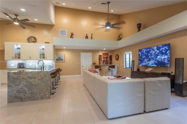 tiled living room featuring ceiling fan, sink, and a high ceiling