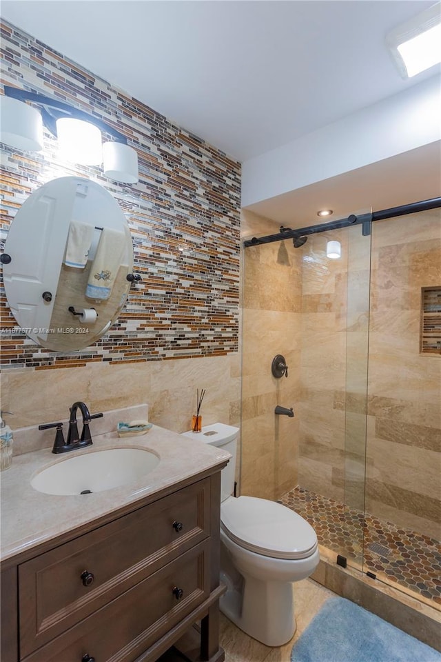 bathroom featuring tile patterned flooring, toilet, a shower with door, vanity, and tile walls