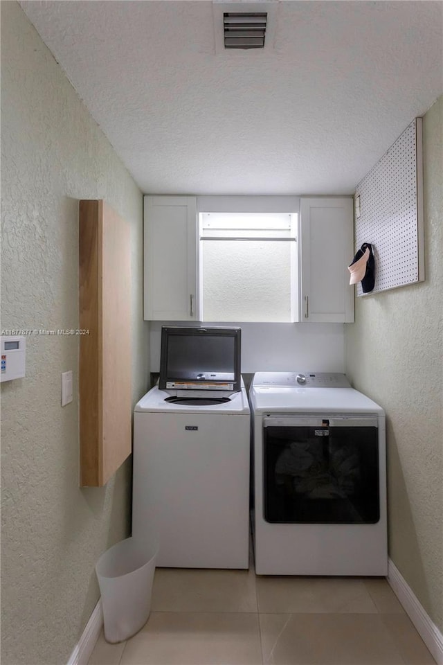 laundry room with cabinets, light tile patterned floors, a textured ceiling, and separate washer and dryer