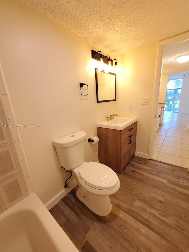 bathroom with a bath, a textured ceiling, hardwood / wood-style floors, toilet, and vanity