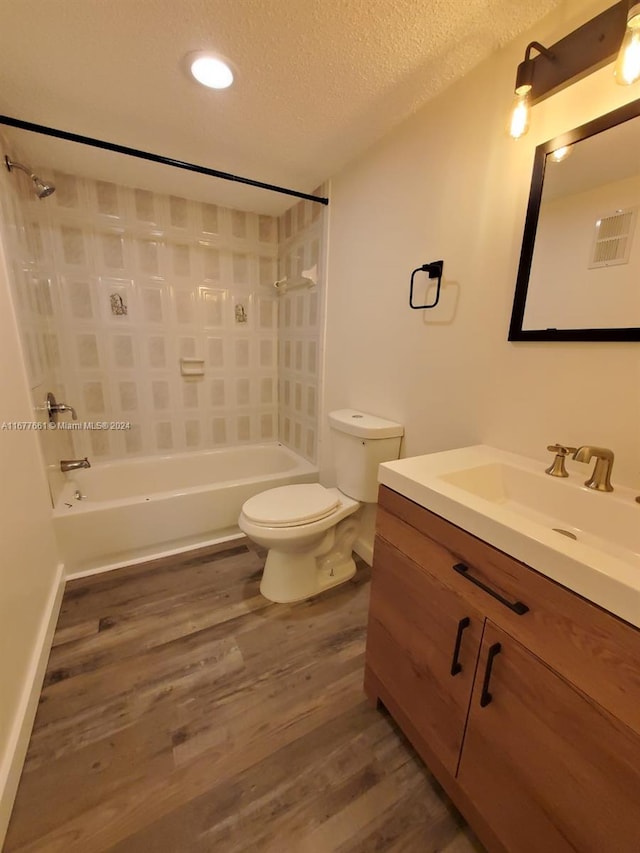 full bathroom featuring a textured ceiling, hardwood / wood-style flooring, toilet, vanity, and tiled shower / bath combo