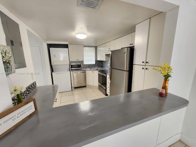 kitchen with white cabinetry, backsplash, stacked washer and dryer, electric panel, and stainless steel appliances