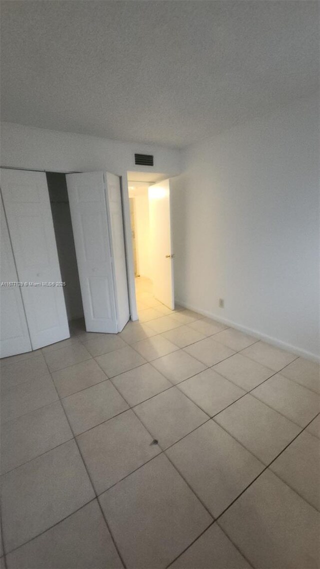 unfurnished bedroom featuring light tile patterned flooring, a textured ceiling, and a closet