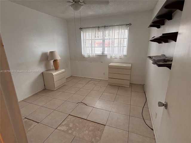 empty room with ceiling fan, a textured ceiling, and light tile patterned flooring