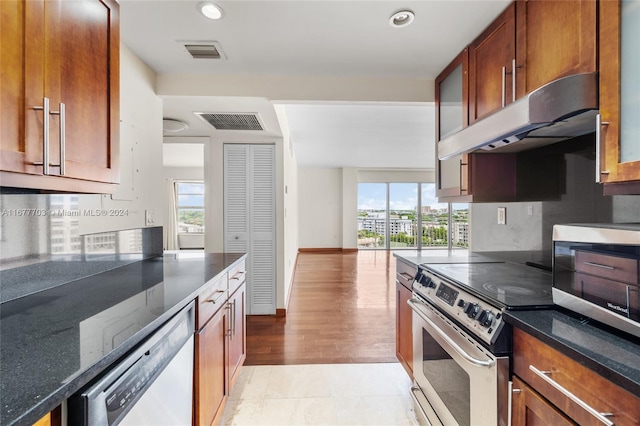 kitchen featuring stainless steel appliances, decorative backsplash, light hardwood / wood-style flooring, and dark stone counters