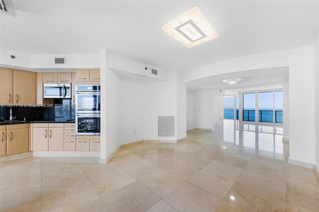 kitchen with appliances with stainless steel finishes, backsplash, sink, light brown cabinets, and a water view