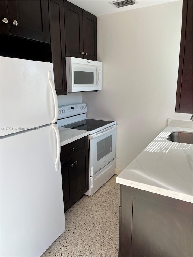 kitchen with white appliances, light stone countertops, dark brown cabinets, and sink