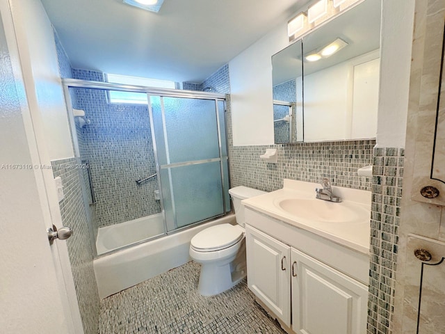 full bathroom with tile walls, vanity, bath / shower combo with glass door, tile patterned flooring, and toilet