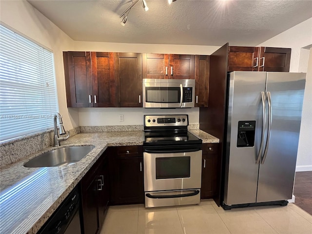 kitchen with sink, light stone countertops, light tile patterned floors, appliances with stainless steel finishes, and a textured ceiling