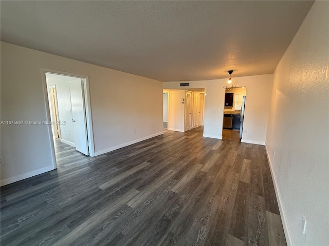 unfurnished living room with a textured ceiling, dark wood finished floors, visible vents, and baseboards