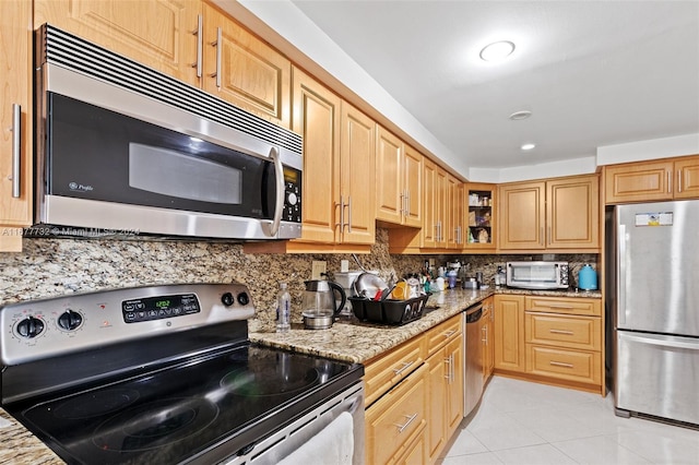 kitchen featuring tasteful backsplash, light stone countertops, light tile patterned floors, and appliances with stainless steel finishes