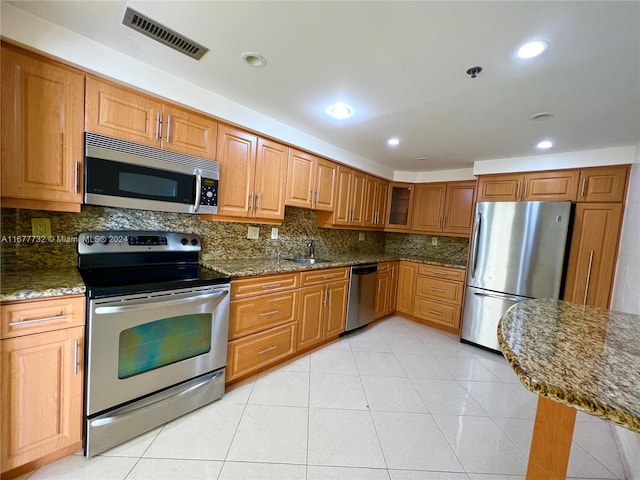 kitchen featuring dark stone counters, sink, decorative backsplash, light tile patterned floors, and stainless steel appliances