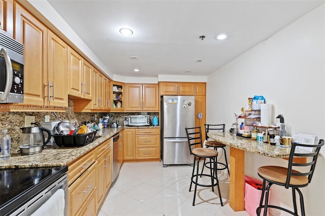 kitchen featuring light stone countertops, backsplash, a breakfast bar area, light tile patterned flooring, and appliances with stainless steel finishes