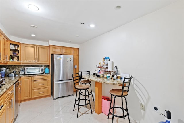 kitchen featuring a kitchen bar, appliances with stainless steel finishes, decorative backsplash, light stone countertops, and light tile patterned floors