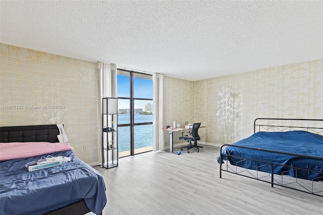 bedroom with wood-type flooring, a water view, floor to ceiling windows, and access to outside