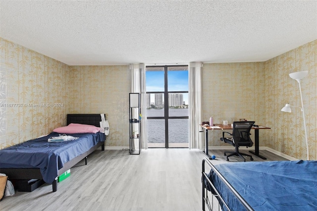 bedroom featuring hardwood / wood-style floors, a textured ceiling, and a wall of windows