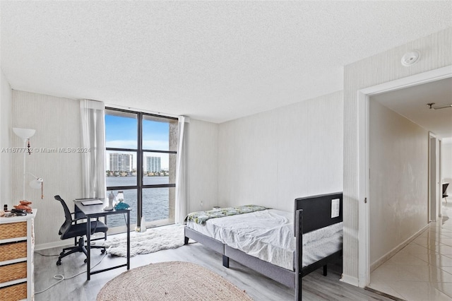 bedroom with a textured ceiling, a water view, light hardwood / wood-style flooring, and expansive windows