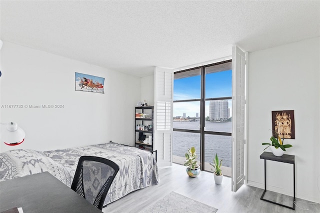 bedroom with expansive windows, a water view, a textured ceiling, and light wood-type flooring