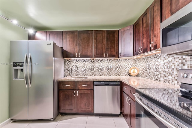 kitchen featuring dark brown cabinets, light stone counters, backsplash, appliances with stainless steel finishes, and sink