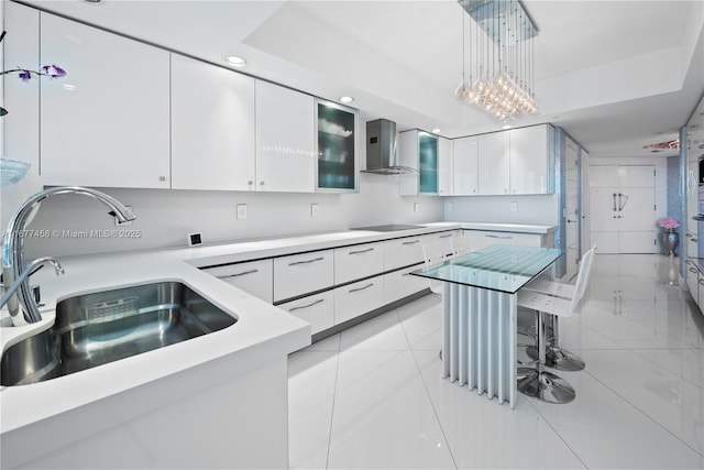 kitchen featuring a sink, light countertops, white cabinets, pendant lighting, and wall chimney range hood