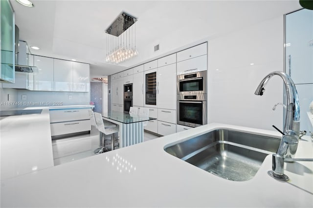 kitchen with modern cabinets, pendant lighting, a sink, white cabinetry, and stainless steel double oven