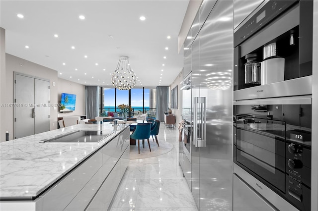 kitchen featuring a large island, light stone countertops, white cabinetry, an inviting chandelier, and appliances with stainless steel finishes