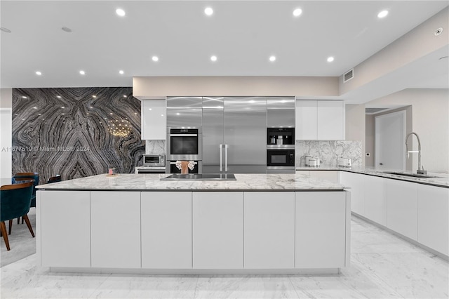 kitchen featuring light stone counters, tasteful backsplash, sink, and white cabinets