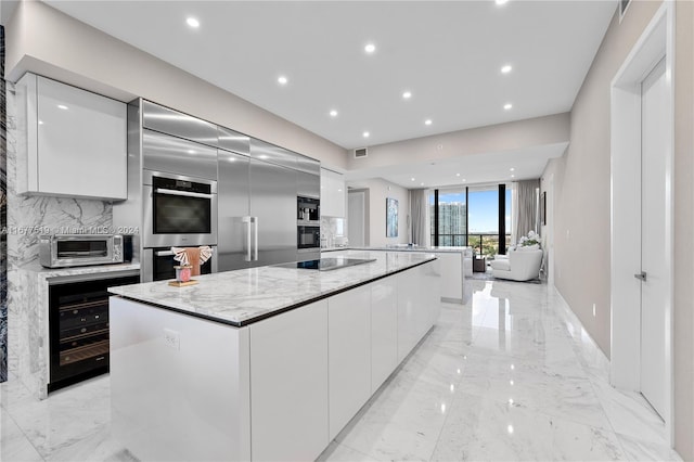 kitchen featuring a large island, light stone countertops, white cabinetry, and stainless steel double oven