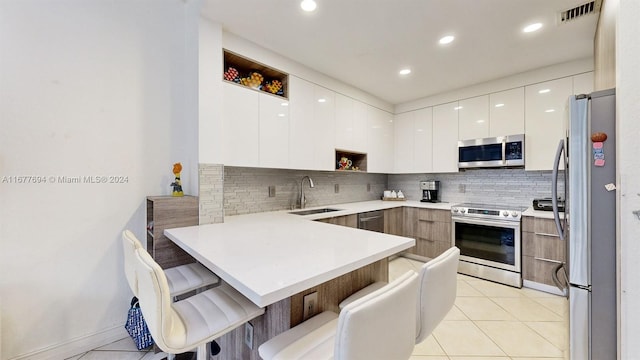 kitchen featuring appliances with stainless steel finishes, sink, kitchen peninsula, a kitchen breakfast bar, and white cabinetry