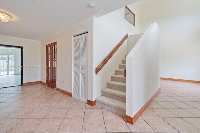 stairs with tile patterned floors, french doors, and a textured ceiling